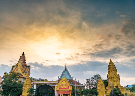 Golden colored sky as the sun sets behind the famous tourist site of the Cambodian capital city.beautiful Khmer pagodas blend with the vibrant gold and blue hues of the partially obscured sun.の写真素材