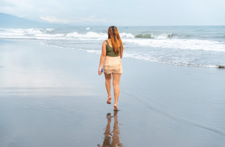 Holding her phone for selfies,on a beach near Manila at dusk,aimlessly strolling the warm shoreline waters,along smooth sands,having fun,dancing around,kicking the gentle waves as they roll in.の写真素材