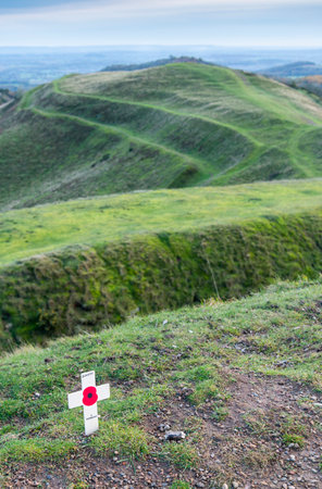On November 11th,on Armistice day,a memorial tribute,red poppy symbol,placed in the soil atop the ancient Hill Fort,by an anonymous hill walker,the southern Malvern hills beyond.の写真素材