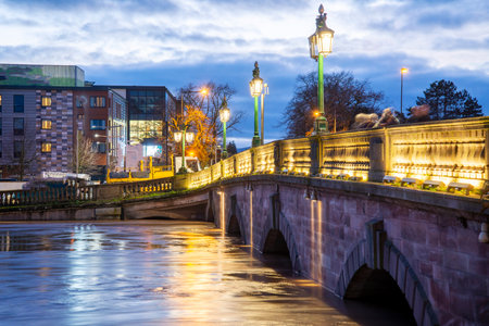 At sunset,after stormy, wet weather,significant torrents of rain water passing under the lluminated historic bridge,along the Severn,after pouring in from surrounding areas,bursting it's banks.の写真素材