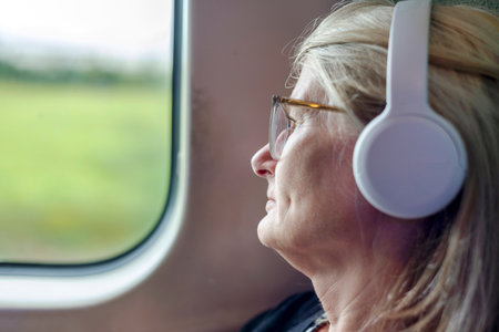 A blonde female traveling on a fast long distance train,listening to an audiobook on her large noise...