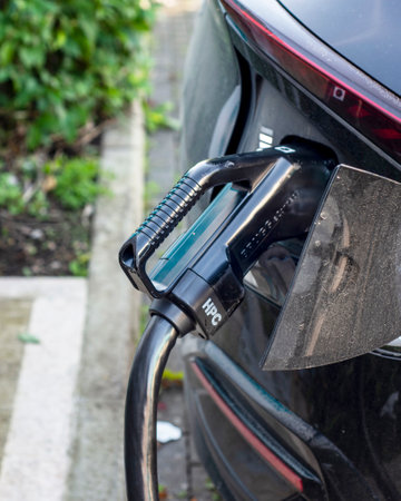 Parked domestic electric car,with charging connector attached ,being charged at a public electric vehicle charging location,situated within a public railway station car park.の写真素材