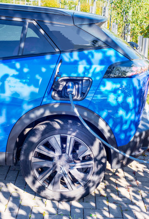 Parked EV,domestic car,with charging connector attached ,being charged at a public electric vehicle charging location,situated within a railway station car park.の写真素材