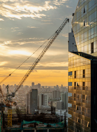 Abstract view of a high construction crane,with hook dangling,ponting towards a reflective,glass...