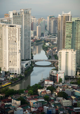 The Pasig River,with high,tall modern buildings lining the riverbanks, road bridges crossing the...