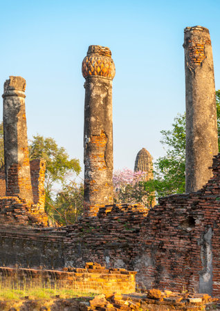 Ancient walls and columns at the historic site,with Buddhist pagoda,stood amongst trees,bathed in the light of sunset,with clear blue skies.の写真素材