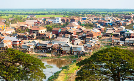In late afternoon sunlight, standing next to a water pond, simple dwellings viewed from Phnom Krom hilltop temple, the area becomes flooded in rainy season.の写真素材