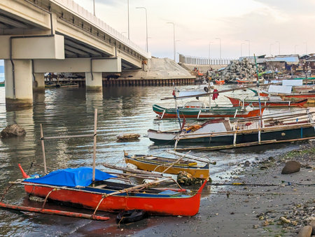 At sunset the concrete flyover takes traffic over a small stretch of water,next to fishing boats,rocks and a small beach with small huts belonging to local people.の写真素材
