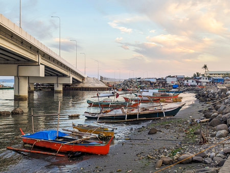 At sunset the concrete flyover takes traffic over a small stretch of water,next to fishing boats,rocks and a small beach with small huts belonging to local people.の写真素材