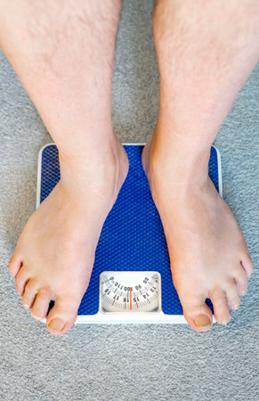 Users eye view of domestic spring scales,looking down at the bare feet and legs of a white male,to view the rotating dial,showing a readout in stones,pounds and kilograms.の写真素材
