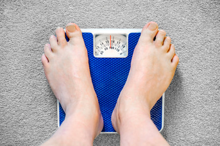 Users eye view of domestic spring scales,looking down at the bare feet and legs of a white male,to view the rotating dial,showing a readout in stones,pounds and kilograms.の写真素材