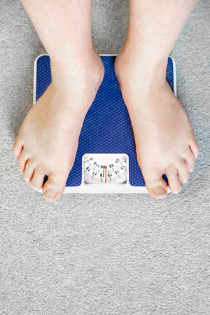 Users eye view of domestic spring scales,looking down at the bare feet and legs of a white male,to view the rotating dial,showing a readout in stones,pounds and kilograms.の写真素材