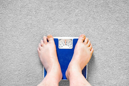 Users eye view of domestic spring scales,looking down at the bare feet and legs of a white male,to view the rotating dial,showing a readout in stones,pounds and kilograms.の写真素材