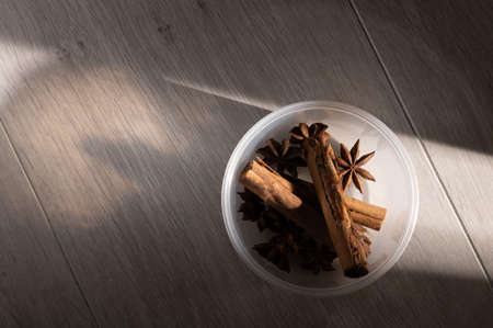 Cinnamon and star anise in an opaque dish on a light wood tableの写真素材