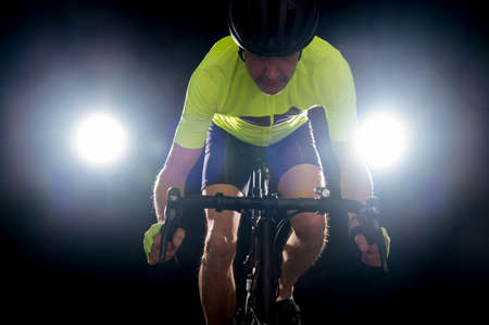 Cyclist back lit  in a yellow jersey and black helmet on a black backgroundの写真素材
