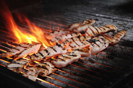 chicken fillets cooking on flaming charcoal grillの写真素材