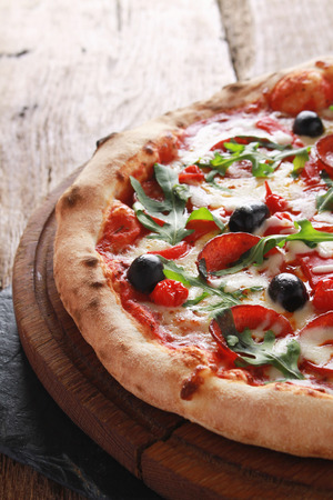 whole fresh baked pizza with olives and salamiの写真素材