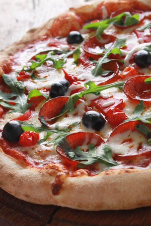 whole fresh baked pizza with olives and salamiの写真素材