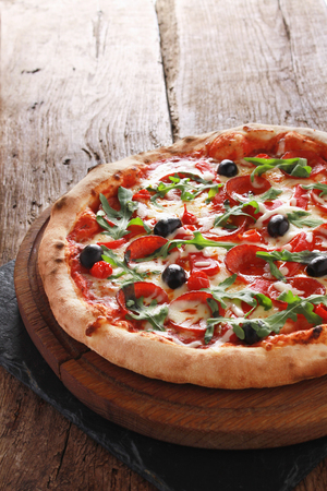 whole fresh baked pizza with olives and salamiの写真素材