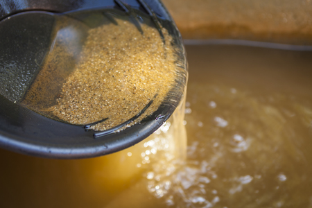Close up of gold panning pan with sifting sand. Shallow depth of field with focus on sand flowing over edge of pan into water.の写真素材
