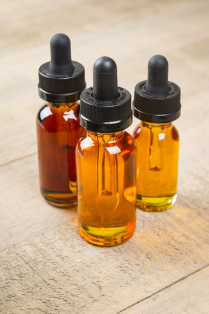 Vaping e-cig juice bottles over wood background. E-Juice in bottle with child proof lid.の写真素材