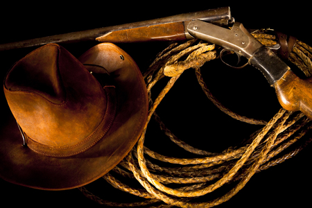 Old Western still life with gun, rope and cowboy hat on a dark background.