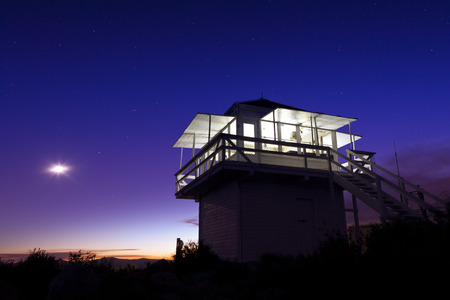 Lit Fire lookout at night with sunset and moon in the sky.の写真素材