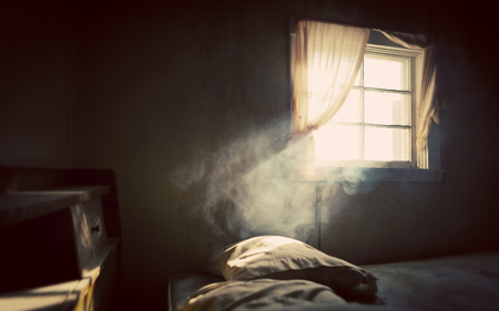 Vintage treated old abandoned bedroom with smoke lit by an open window with curtainsの写真素材