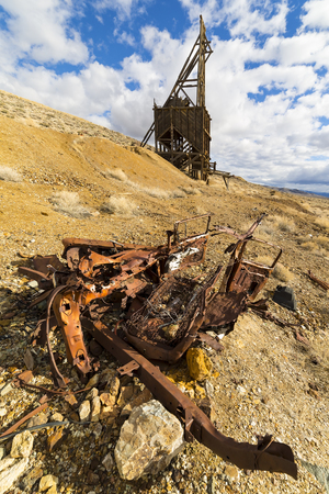 Ghost town mining head frame in the Nevada desert with wrecked car in the foreground.  Sky is blue with clouds.の写真素材