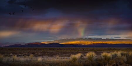 Stormy Sunset with rain and rainbow in the desert with light on mountain range.  Fallon, NVの写真素材