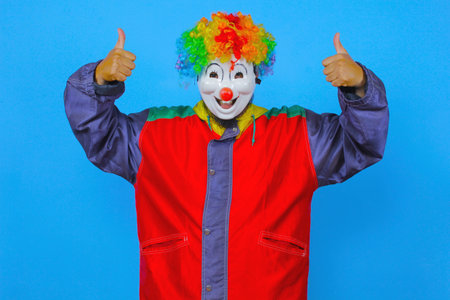 Portrait of a funny clown showing thumbs up isolated on blue backgroundの写真素材