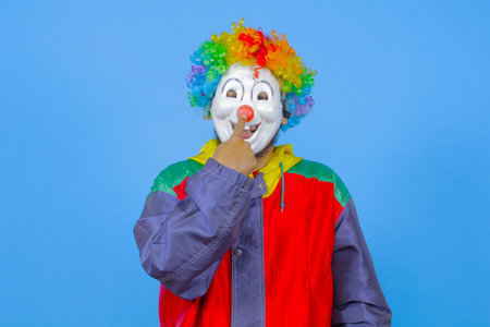 Clown with colorful wig and red jacket on blue background. Studio shot.の写真素材