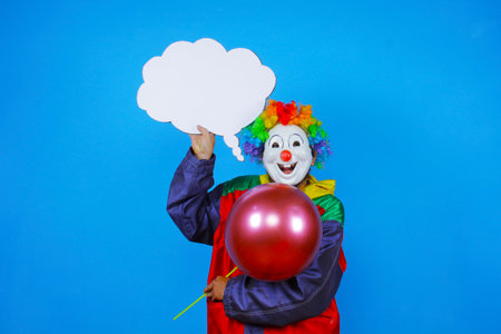Clown with speech bubble and balloon isolated on blue background. Studio shot.の写真素材