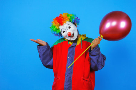 Clown with a balloon on a blue background in the studio.の写真素材