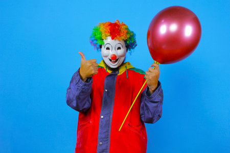 Clown with red balloon and thumb up on a blue background.の写真素材