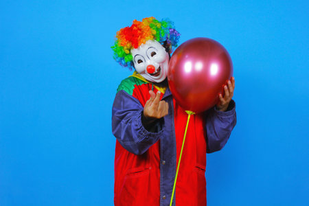 Portrait of a clown with a red balloon in his hand on a blue backgroundの写真素材