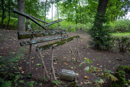 Old broken bench in Latvia cemetery graveyard with peeling paint. metak legs, empty glass jar on groundの写真素材