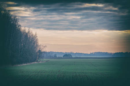 landscape with forest, green meadow and house in distance.の写真素材