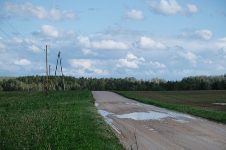 country road with puddles on it and blue sky with clouds