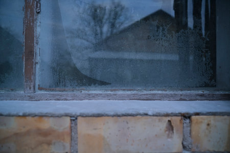The window is covered with frost. Reflection of house in window