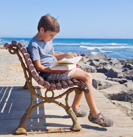 boy  reading book on summer bench on sea coastの写真素材