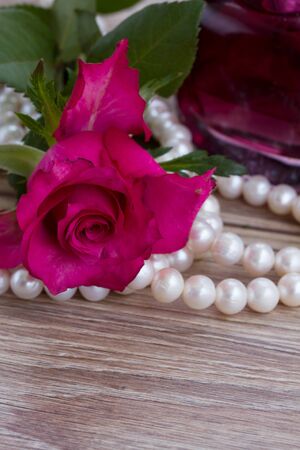 pink rose with pearl necklace and parfume bottle on wooden tableの写真素材
