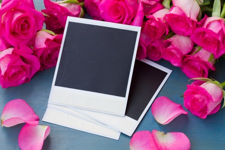 fresh pink roses on wooden table with blank instant photos