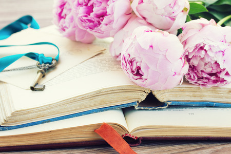 pile of vintage old books with fresh peony flowers stacked on tableの写真素材
