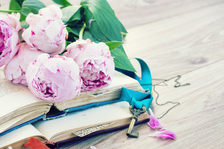 pile of vintage old books with fresh pink peony flowers and key stacked on tableの写真素材