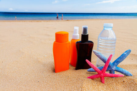 bottle of cool water with suntun creams on sandy beach by sea sideの写真素材