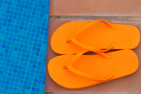 orange flip flops left on pool edgeの写真素材