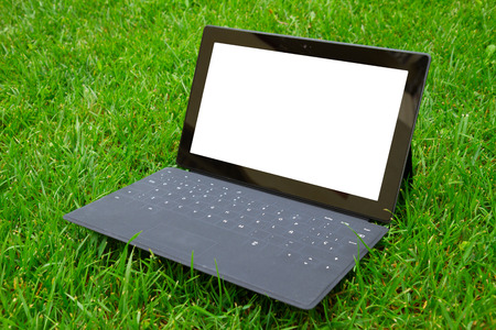 Tablet with keyboard on fresh green grass, copy space on display