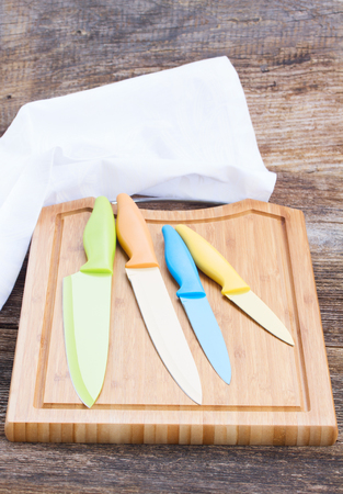 set of colorful ceramic  knives on wooden cutting boardの写真素材