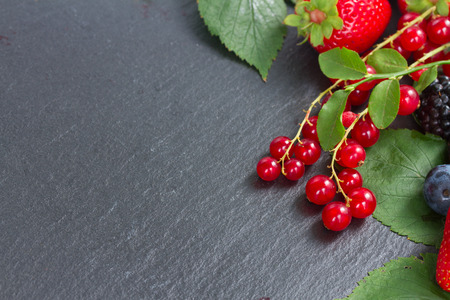 pile of fresh ripe berries with green  leaves with copy space   on black stoneの写真素材